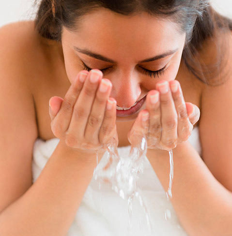 Woman with dark hair who appears to be washing her face.