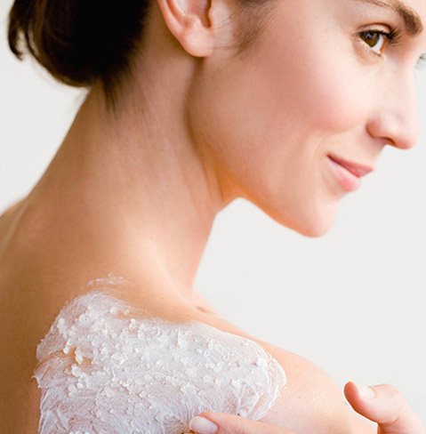Back of a woman with fair skin who has some kind of cream on the back of her right shoulder right.